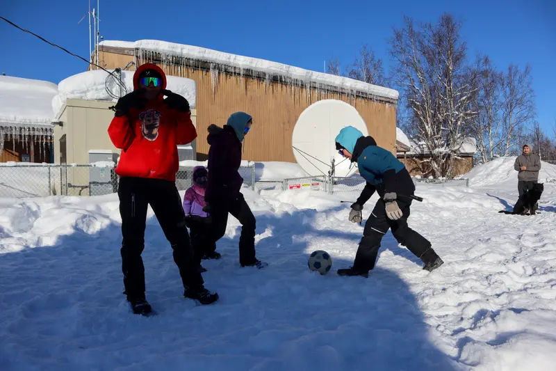 Children bundled up in cold-weather gear play soccer in the snow.