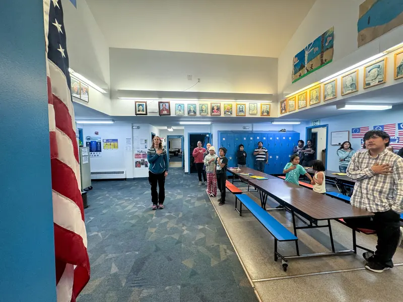 Students and staff stand with hands on hearts in the area where they eat lunch.