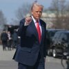 In this photo, President Trump is walking outdoors with his right fist raised to about shoulder height. He's wearing a dark blue suit and red tie.