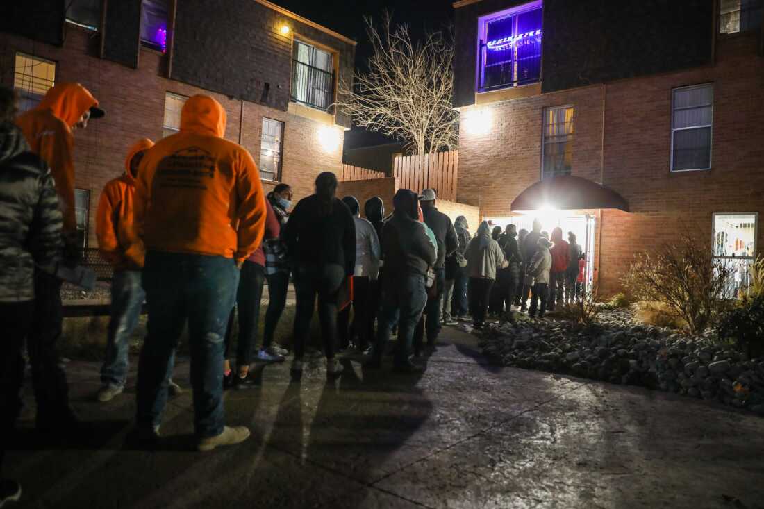 A vaccination event in Dec. 2021 shows dozens of people lined up outside in the dark, waiting to get a shot.