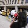 In this photo, demonstrators holding signs are standing outside the U.S. Department of Education's building in Washington, D.C., protesting against planned mass layoffs at the agency. In the foreground, a person is speaking into a megaphone.